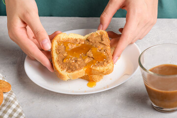 Female hands holding a sandwich with honey and peanut butter spreading on piece of white bread toast, close up. Typical snack food, food lifestyle, domestic life, american breakfast