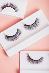 Different fake eyelashes in boxes on trendy pastel pink background. Makeup accessories and beauty cosmetics products for women. Top view, flat lay.