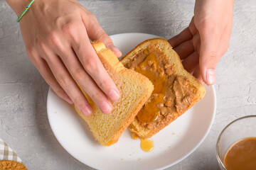 Female hands making a sandwich with honey and peanut butter spreading on piece of wheat bread toast, close up. Typical snack food, food lifestyle, domestic life, american breakfast