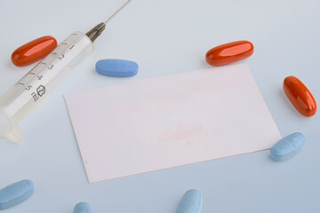 A card, pills, a syringe on a light background. Copy space