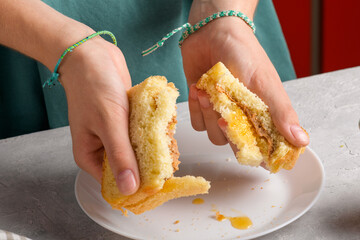 womans hands breaking a sandwich with honey and peanut butter of wheat bread on white plate, to have a breakfast, close up. Typical snack food, food lifestyle, american breakfast, ready to eat