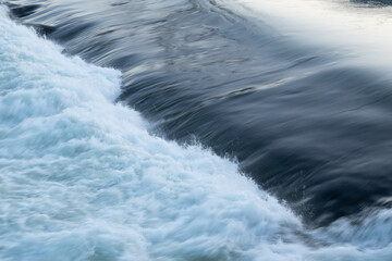 Rapid water flow over barrier, river overflow over dam close up with splash and foam, abstract...