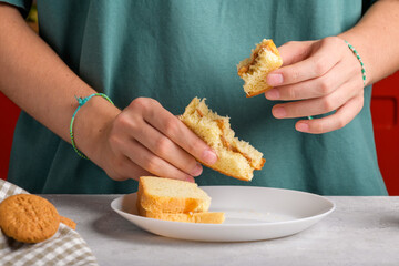 Female hands holding a bitten peanut butter sandwich with honey of wheat bread, have a breakfast. Woman faceless in petrol green colored t-shirt with bitten sandwich. Typical morning breakfast