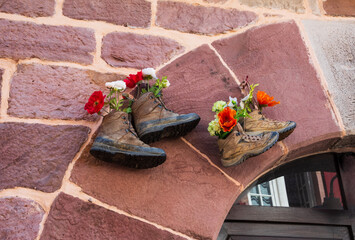 Old hiking shoes using as flower pot hanging stone wall house. Hiking background. Lifestyle, natural leaving, travel, sustainable consumption concepts