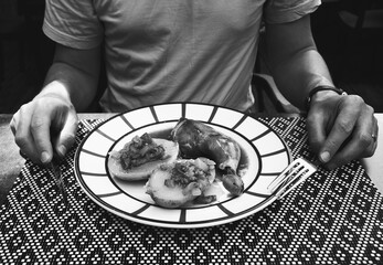 Man preparing to eat his meal at traditional French Basque country restaurant. Chicken leg, baked potato with ratatouille aesthetically served. Black white historic photo.