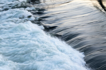 Rapid water flow over barrier, river overflow over dam close up with splash and foam, abstract landscape pastel blue