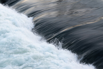 Rapid water flow over barrier, river overflow over dam close up with splash and foam, abstract landscape pastel blue
