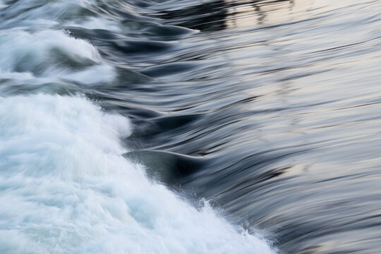 Rapid water flow over barrier with silky surface, river overflow over dam close up with splash and foam, abstract landscape pastel blue