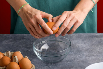 A woman's hand cracking an egg into a clear glass bowl in the gray kitchen table, the process of cooking, Lifestyle, close up