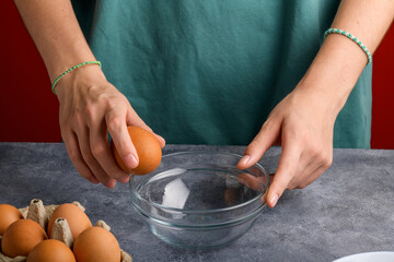 A woman's hand cracking an egg into a clear glass bowl in the gray kitchen table