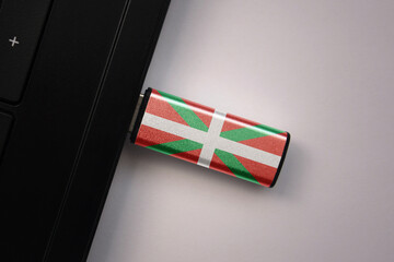 usb flash drive in notebook computer with the national flag of basque country on gray background.