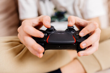 Close-up of a young gamer's hands operating a PS controller. Home game console, modern technology,...