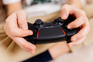 Close-up of a young gamer's hands operating a PS controller. Home game console, modern technology,...