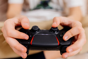 Close-up of a young gamer's hands operating a PS controller. Home game console, modern technology,...