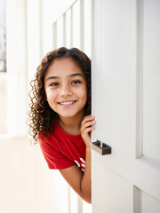 Cheerful teenage girl with curly hair peeking out of door