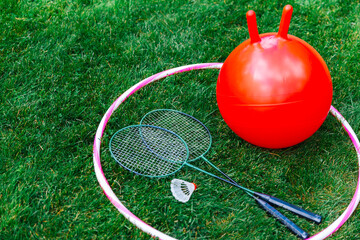 leisure games, sport equipment and toys concept - bouncing ball or hopper, hula hoop and set of badminton rackets with shuttlecock on grass - 755862134