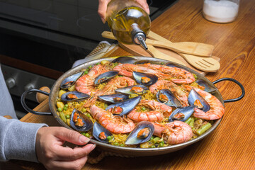 Pouring olive oil into a seafood paella, enhancing the flavors of this classic Spanish dish,...
