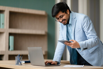 Middle Eastern businessman texting on cellphone using laptop at office