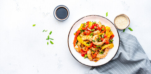 Spicy stir fry shrimps with colorful paprika, green peas, onion and sesame seeds with ginger, garlic and soy sauce in white bowl on kitchen table background, top view banner