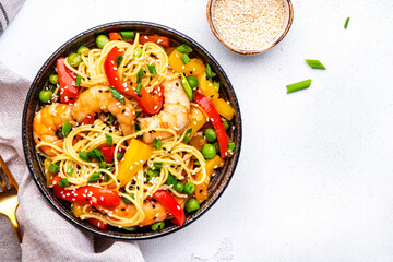 Spicy stir fry noodles with shrimps, colorful paprika, green pea, green onion and sesame seeds with ginger, garlic and soy sauce. White table background, top view