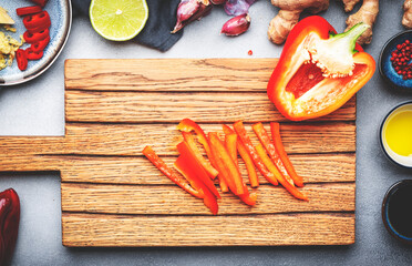 Food and cooking background. Wooden cutting board with chopped paprika. Zucchini, raw vegetables, spices and ingredients for cooking vegan Asian dishes with ginger, garlic, soy sauce, top view