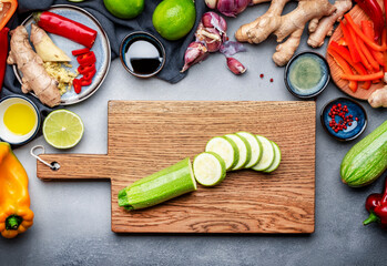Food and cooking background. Gray table with chopped zucchini. Paprika, vegetables, spices and ingredients for cooking vegan Asian dishes with ginger, garlic, soy sauce, top view
