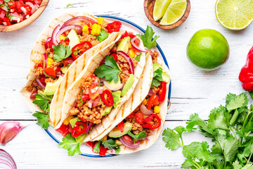 Tacos with ground beef, sweet corn, red beans, tomato salsa sauce and red onion in corn tortillas on plate. Mexican cuisine. Taco party menu. White table background, top view