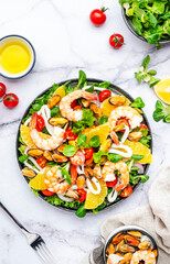 Delicious salad with seafood, oranges, lamb lettuce and olive oil with lemon juice dressing, marble table background, top view