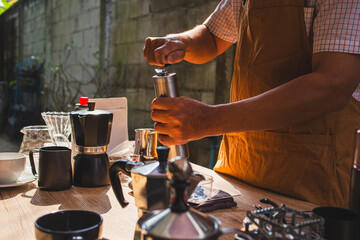 people is grinding coffee beans with manual stainless steel grinder to make black coffee machine, brewing equipment or coffee drip set Dripper on a wooden table In the kitchen at home in the morning