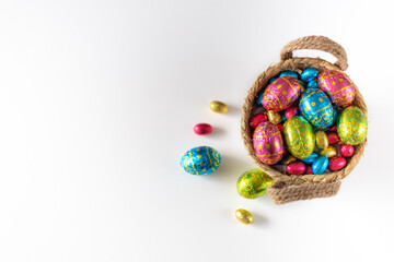 Easter eggs in basket with white background on white table. Studio lighting colorful easter decorated eggs for egg hunt with wicker basket and flowers. Banner for web and composition. Top view
