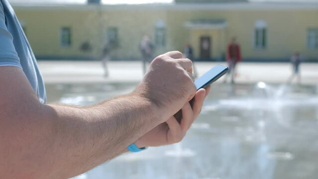 Closeup of man typing text message on smartphone or hands using mobile phone in the park there is a backdrop of people passing by.