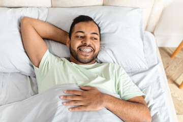 Top view of happy african american guy laying in bed