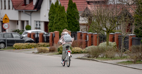 Fototapeta na wymiar Girl Rides Bicycle Among Private Houses In Europe During Spring, View From Behind