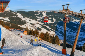 Tuinposter A vibrant ski resort, bathed in sunlight with skiers, snowboarders, and a red gondola lift against a picturesque mountain backdrop. Ideal for concepts of winter sports, vacation, and adventure © Александр Бочкала