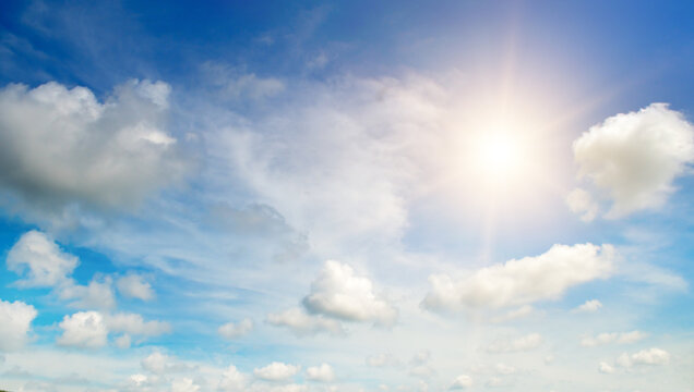 There are white cumulus clouds and a bright sun in the blue sky.