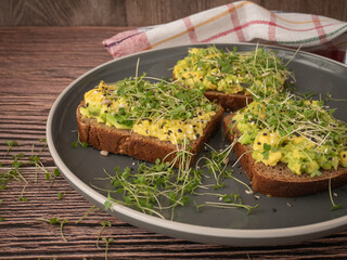 Micro-green arugula sprouts on an avocado sandwich on a gray plate on a wooden background. The concept of proper nutrition, low-calorie snacks and weight loss
