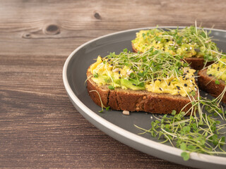 Micro-green arugula sprouts on an avocado sandwich on a gray plate on a wooden background. The concept of proper nutrition, low-calorie snacks and weight loss