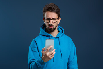 Skeptical man wearing glasses looking at smartphone screen