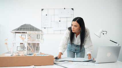 Young beautiful caucasian architect puts blueprint on the table and compare with house model while...