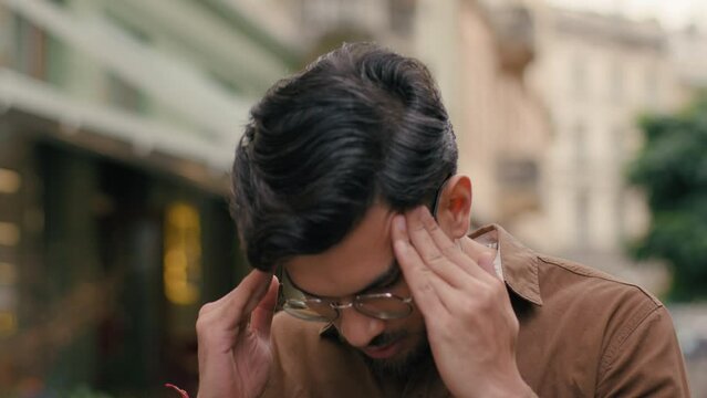 Annoyed angry mad stressed Indian Arabian ethnic male student man guy businessman client customer furious business fail loss dissatisfaction frustration headache touch holding head outside city street