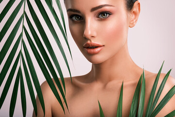 Young beautiful woman with green leaves near face and body. Skin care beauty treatments concept.  Closeup girl's face with green leave. White model with clean, health skin of face - posing at studio