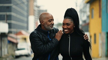 African American Mature father walks forward with arm around teenage daughter in urban street together giving parental advice. Parent and teen child bonding time