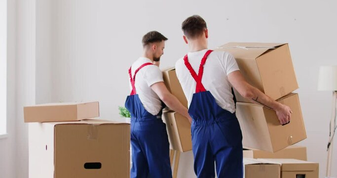 Two mover men from the relocation service help a woman client move into new home, cheerfully carrying cardboard boxes. The staff members are smiling, providing friendly and efficient service.