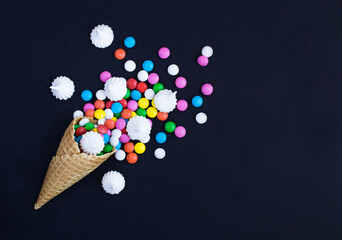 Ice cream cone with colored candy dragees and white meringue on the black background. Copt space. Top view.