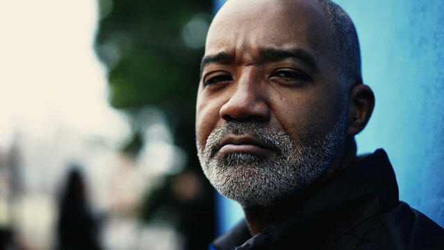 Serious Middle-aged South American hispanic black man close-up face looking at camera in urban environment. Gray hair bearded bold 50s person portrait with concerned expression