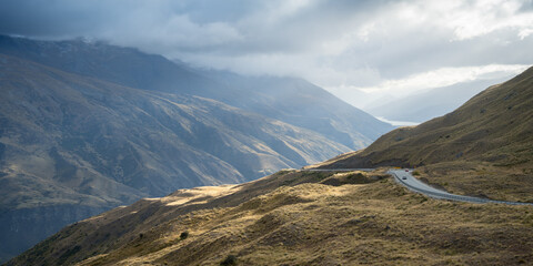 Cars passing curvy road leading through mountains pass in alpine environment, New Zealand