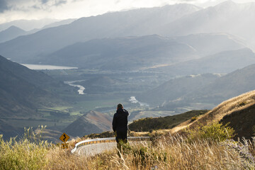Fototapeta na wymiar Man taking photograph of beautiful river valley surrounded by mountains with his phone, New Zealand