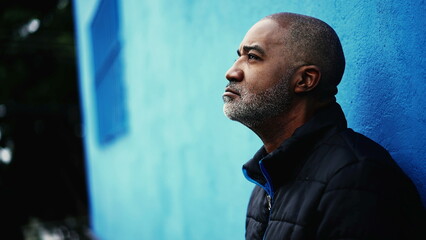 One pensive middle-aged black man standing outside in city street gazing upwards in deep...