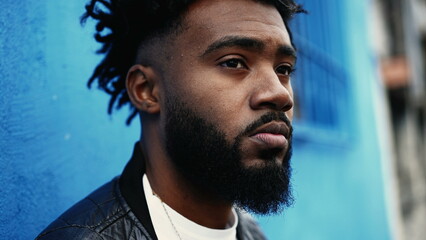 One pensive young black man standing in city street gazing with thoughtful expression. African...