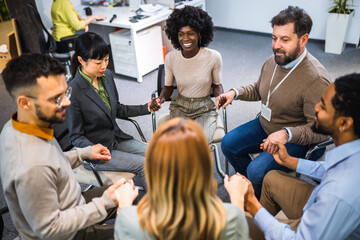 Group of people sitting in a circle holding hands and participate in a support meeting. Healthcare...